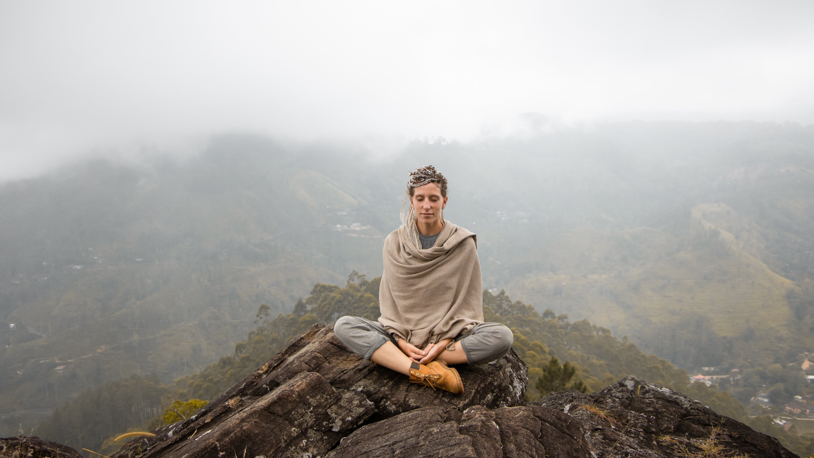 Mujer meditando sentada sobre una roca en la montaña, entre la niebla